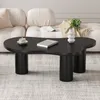A black, cloud-shaped coffee table with a book and a cup of coffee on it, placed in front of a cream-colored sofa. Voir les images du produit