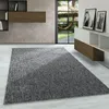 A modern living room with a grey rug in the foreground, a window with a view of a garden and hammock in the background, and wall-mounted shelves and a cabinet. Produktbild-Vorschau