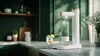 A kitchen counter with a sparkling water maker, a glass of sparkling water with lemon, and some kitchen decor in the background. Produktbild-Vorschau