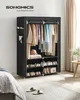 A black fabric wardrobe with clothes and shoes inside, placed in a bedroom setting. Produktbild-Vorschau