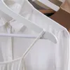 Close-up of white clothing hangers holding white garments and a beige garment. Produktbild-Vorschau