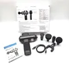 A massage gun and its accessories are laid out on a white surface, with the product's packaging in the background. Produktbild-Vorschau