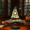A stained glass witch hat lamp sits on a wooden desk next to a cup of coffee and a book. Produktbild-Vorschau
