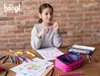 A young girl is drawing at a table with art supplies. Anteprima dell’immagine prodotto