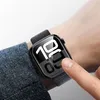 A person's wrist wearing a smartwatch with a dark fabric band. The smartwatch screen displays the time. Produktbild-Vorschau