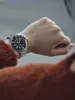 A person wearing a watch on their wrist, with part of their clothing visible. Náhled obrázku produktu