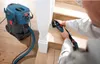 A person is using a Bosch multi-tool to sand a wooden staircase, with a Bosch vacuum cleaner attached. Náhled obrázku produktu
