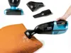 A hand holding a handheld vacuum cleaner with various attachments, demonstrating its use on an orange cushion. Produktbild-Vorschau