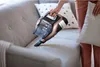 A person is using a cordless vacuum cleaner to clean a sofa. Produktbild-Vorschau