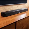 A black Bose soundbar is placed on a wooden cabinet in front of a textured wall and a television. Anteprima dell’immagine prodotto