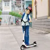 A young boy wearing a helmet and backpack is riding an electric scooter on a street. Náhled obrázku produktu