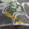 A close-up view of a white floral pattern overlaying a bouquet of sunflowers and greenery, with text visible underneath. Produktbild-Vorschau