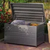 An outdoor storage box filled with cushions and a rolled blanket, placed on a patio with plants in the background. Produktbild-Vorschau
