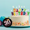 A birthday cake with "Happy Birthday" candles and a "30 Birthday Queen" magnet next to it. Produktbild-Vorschau
