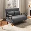 A dark gray sofa bed with two pillows is placed in a living room setting, near a window and a fireplace. Voir les images du produit