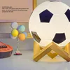 A soccer ball-shaped lamp with a wooden stand, next to a colorful balloon-like lamp and a guitar. Produktbild-Vorschau