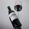 A bottle of red wine and a glass of red wine are placed on a reflective surface against a light gray background. Produktbild-Vorschau