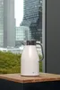 A white alfi thermos jug sits on a wooden surface in front of a window with a city view. Anteprima dell’immagine prodotto