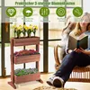A woman is reading a book while sitting in a chair next to a three-tiered wooden planter filled with flowers. Náhled obrázku produktu