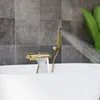 A gold bathtub faucet with a waterfall spout and a handheld showerhead is shown filling a white bathtub. The background is tiled with gray squares. Náhled obrázku produktu