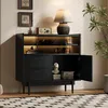 A black sideboard with LED lighting, displaying decorative items and books, in a well-lit room with a plant and artwork on the wall. Produktbild-Vorschau