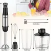 A person is using an immersion blender in a glass of orange juice, with various accessories and fruits displayed around. Produktbild-Vorschau