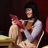 A young woman is sitting and using a pink tablet with a stylus. Produktbild-Vorschau