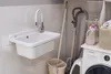 A laundry room or utility area with a sink, washing machine, vacuum cleaner, and cleaning supplies. Anteprima dell’immagine prodotto