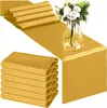 A stack of folded gold satin table runners and a gold satin table runner laid out on a surface with a vase of flowers. Anteprima dell’immagine prodotto