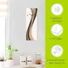 A wall clock with a wavy abstract design is displayed on a white wall, with kitchen items visible on a shelf below. To the right, a green panel highlights product features with icons and text. Produktbild-Vorschau