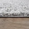 A close-up view of a gray shaggy rug on a wooden floor. Produktbild-Vorschau
