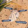 A bird feeder shaped like a cone, made of seeds and fat, is placed on a burlap cloth surrounded by sunflower seeds. It is decorated with a twine bow and has four labels pointing to its features. Produktbild-Vorschau