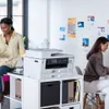 Two women are in an office environment with a printer on a shelf. Produktbild-Vorschau