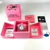 A pink Swatch watch box and its contents are displayed on a white surface. Voir les images du produit