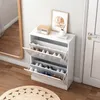 A white shoe cabinet is placed next to a white door and a large mirror, with a rug on the wooden floor. Podgląd zdjęcia produktu