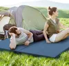A couple relaxing on camping mats in front of a tent in a grassy field. Náhľad obrázku produktu