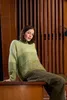 A woman is sitting on a wooden bench in front of a wooden wall. Produktbild-Vorschau