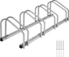 A silver bicycle rack with four slots, shown from a slightly elevated side angle. Four screws and four wall anchors are visible in the bottom right corner. Náhled obrázku produktu