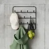 A black metal wall-mounted rack with hooks, holding a white baseball cap, a green hooded garment, and a black mesh bag with yellow fruit. Produktbild-Vorschau