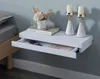 A white floating nightstand with an open drawer next to a bed. Náhled obrázku produktu
