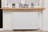 A white radiator cover with a heart pattern is shown in a room, placed against a white wall below a wooden shelf. Produktbild-Vorschau