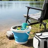 A blue collapsible bucket filled with fishing gear sits on the shore next to a fishing chair and a cooler. Voir les images du produit