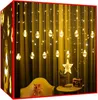 A curtain of warm white LED lights with decorative bulbs hanging in front of a yellow curtain. A star-shaped light fixture and a small radio are on a table in the foreground. Náhled obrázku produktu