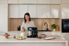 A woman is in a modern kitchen, preparing to use a stand mixer. Náhled obrázku produktu