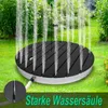 A circular outdoor shower device spraying water upwards in a garden setting. Náhled obrázku produktu