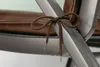 Close-up of a brown braided cord tied in a bow around a gray metal chair frame, with a brown cushion visible in the background. Produktbild-Vorschau