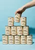A hand is placing a can of black beans on top of a pyramid of other cans. Produktbild-Vorschau
