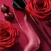 A close-up shot of a glittery red stiletto perfume bottle, surrounded by glittery red roses and heart-shaped candies. Anteprima dell’immagine prodotto