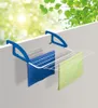 A balcony clothes drying rack mounted on a wall, with two towels hanging on it. The background shows blurred green leaves and sunlight. Produktbild-Vorschau