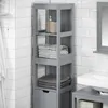 A gray bathroom cabinet with shelves and a drawer, filled with towels and soap dispensers, stands against a white tiled wall. Produktbild-Vorschau